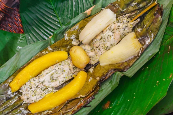 Vista superior de la deliciosa comida típica amazónica, pescado cocinado en una hoja con yuca y plátano, servido en un plato de madera sobre una mesa de madera — Foto de Stock