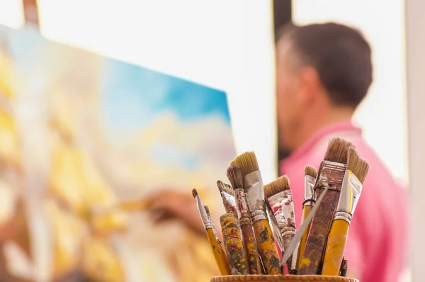 Close-up de frasco de madeira com pincéis de pintura, com pintura homem borrado como fundo — Fotografia de Stock