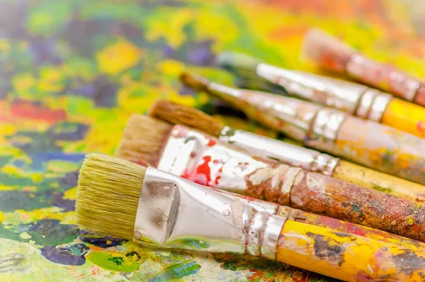 Close up de pincéis de tinta sobre uma paleta de cores em um fundo embaçado — Fotografia de Stock