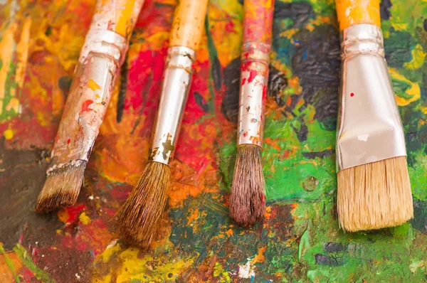 Vista superior de pincéis de tinta sobre uma paleta de cores em um fundo embaçado — Fotografia de Stock