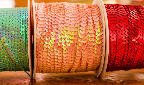 Cose up de rolos brilhantes de fita lantejoulas coloridas, multi-coloridas sobre uma mesa de madeira em um fundo desfocado — Fotografia de Stock