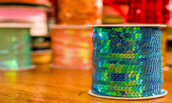 Cose up de rouleaux brillants de paillettes colorées ruban vert, multicolore sur une table en bois dans un fond flou — Photo