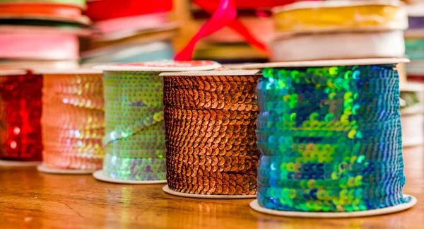 Cose up de rouleaux brillants de ruban paillettes colorées, multicolores sur une table en bois dans un fond flou — Photo