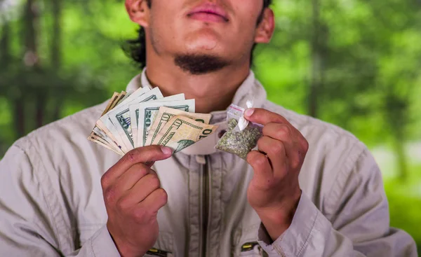 Fechar de um traficante de homens usando óculos escuros, e segurando em suas mãos dinheiro e drogas, tráfico, crime, em um fundo turvo — Fotografia de Stock