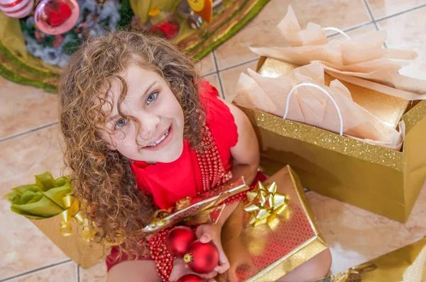Boven weergave van gelukkig meisje draagt een rode blouse en houden een kerst bal, decoratie en cadeau in haar handen, Kerstmis concept — Stockfoto