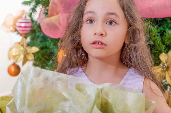 Close up of surprised girl wearing a pink cothes and posing for camera, with a christmas tree behind, christmas and new year concept — Stock Photo, Image