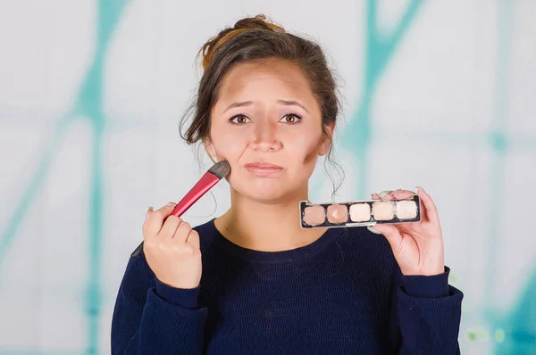 Närbild av unga vackra kvinnan håller en make up palett och göra crazy make-up i hennes ansikte med en borste i en suddig bakgrund — Stockfoto