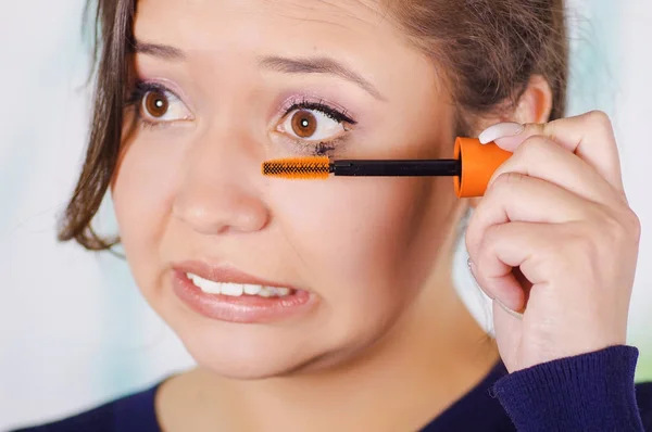 Portrait d'une jeune femme inquiète faisant un gâchis en utilisant un mascara oculaire dans son œil, dans un fond flou — Photo