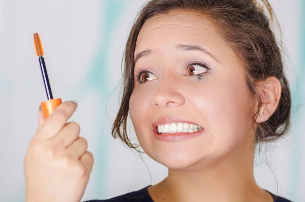 Close-up van bezorgd jonge vrouw doen een puinhoop met behulp van een oog mascara in haar oog, in een onscherpe achtergrond — Stockfoto