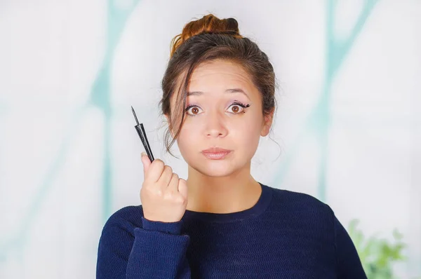 Close-up van de mooie jonge vrouw met een eyeliner in haar hand, in een onscherpe achtergrond — Stockfoto