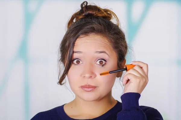 Close-up van verrast jonge vrouw doen een puinhoop met behulp van een oog mascara in haar oog, in een onscherpe achtergrond — Stockfoto