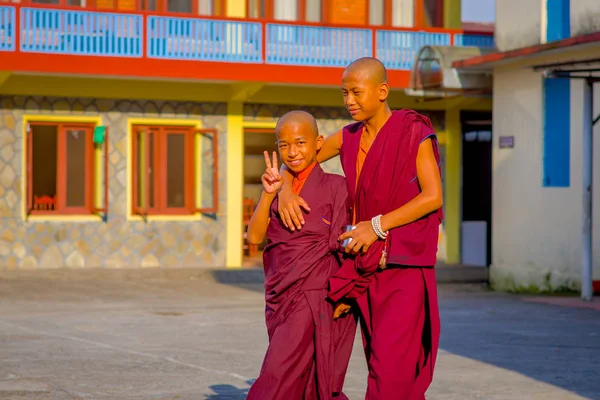 POKHARA, NEPAL - 06 DE OCTUBRE DE 2017: Niños monjes budistas no identificados abrazándose, niño pequeño haciendo una señal de éxito con su mano en el exterior en el asentamiento de refugiados Tashi en Pokhara, Nepal — Foto de Stock