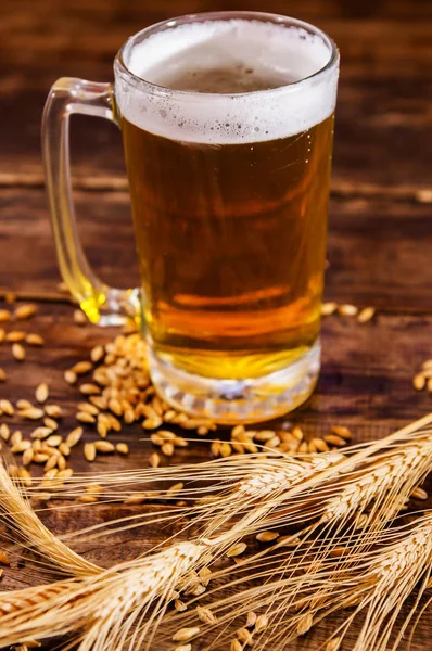 Sopra la vista di una mano che tiene un bicchiere di birra leggera con schiuma, con un ramo di grano e grano su un tavolo di legno — Foto Stock