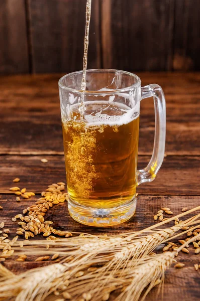 Sopra la vista di una mano che tiene un bicchiere di birra leggera con schiuma, con un ramo di grano e grano su un tavolo di legno — Foto Stock