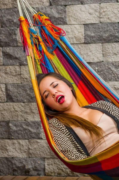 Mujer joven tomando una siesta en una hamaca con la boca abierta, en un fondo borroso — Foto de Stock