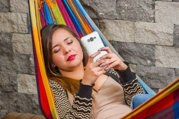 Primer plano de la joven hermosa mujer durmiendo en una hamaca mientras ella está con un teléfono celular en sus manos, en un fondo borroso —  Fotos de Stock