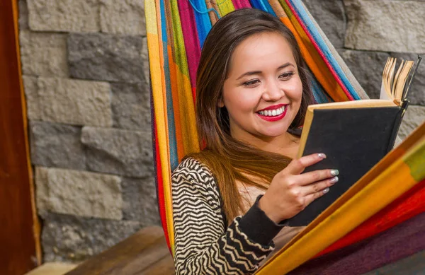 Close up of smiling young beautiful woman reading a book in a hammock, in blurred background — Stock Photo, Image