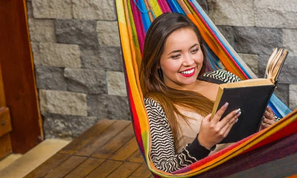 Close up of smiling young beautiful woman reading a book in a hammock, in blurred background — Stock Photo, Image