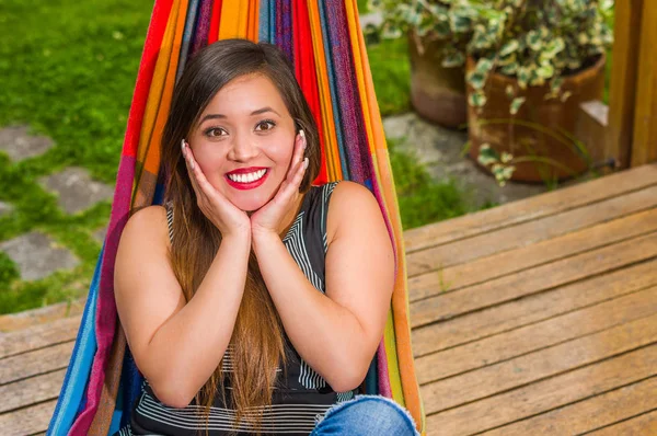 Buiten beeld van lachende jonge mooie vrouw ontspannen in een hangmat met beide handen onder haar kin, op houten natuur achtergrond — Stockfoto