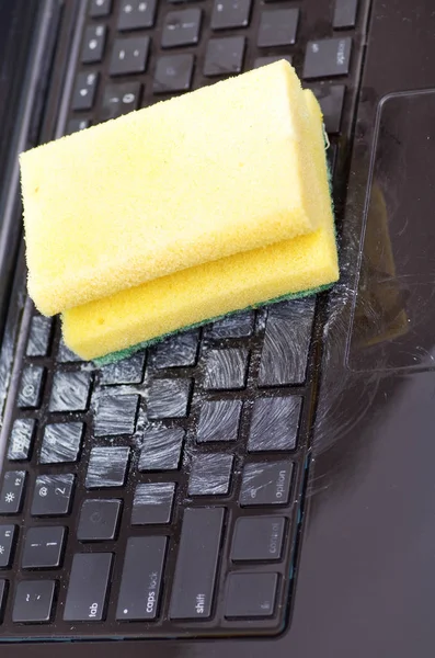 Primo piano del computer portatile con acqua goccia danni liquido bagnato e versare sulla tastiera e utilizzando una spugna gialla con detergente per pulire — Foto Stock