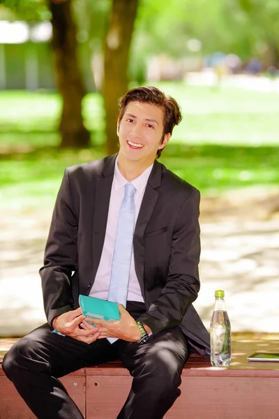 Jeune homme d'affaires souriant portant un costume et tenant un sandwich à l'intérieur d'une boîte de conseil à l'extérieur, dans un fond de parc flou — Photo