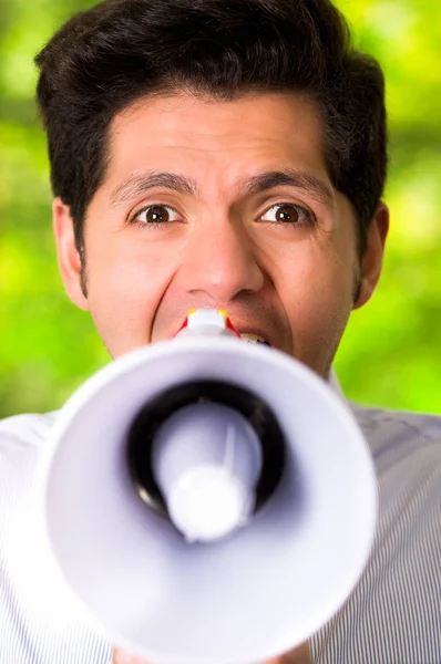 Portret van een knappe man met een megafoon in een wazig groene achtergrond schreeuwen — Stockfoto