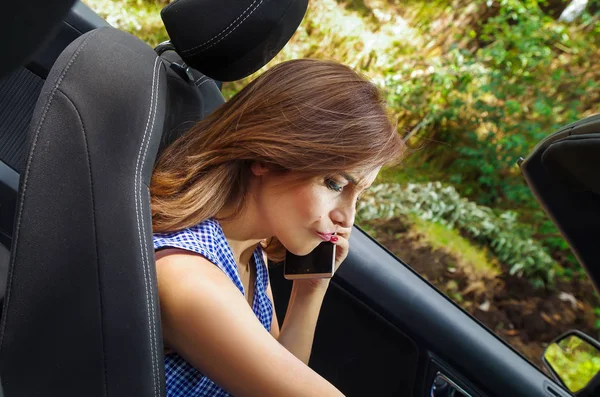 Porträtt av vacker kvinna via hennes mobil insidan svart bilen, samtidigt som hon driver i en suddig natur bakgrund — Stockfoto