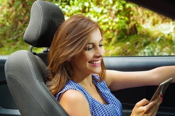 Närbild av vackra kaukasiska kvinna via hennes mobil insidan svart bilen, samtidigt som hon driver i en suddig natur bakgrund — Stockfoto