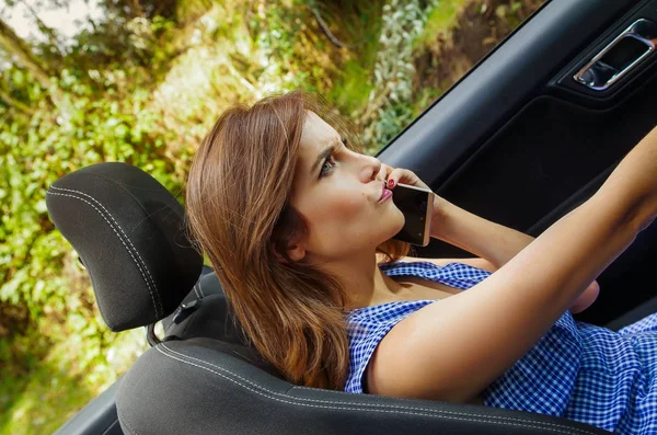 Крупним планом красива біла жінка використовує свій мобільний телефон всередині чорного автомобіля, поки вона їде на розмитому фоні природи — стокове фото
