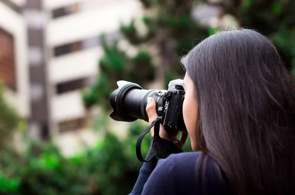 Giovane donna stalking e scattare foto con la fotocamera, all'esterno con uno sfondo ufficio — Foto Stock