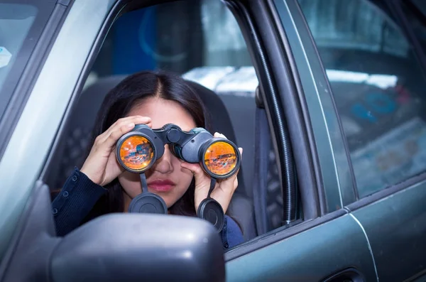 Young woman stalking with a black binoculars inside of her car — Stock Photo, Image