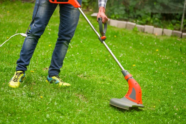 Unga arbetstagare med en sträng gräsmatta trimmer gräsklipparen gräset i en suddig natur bakgrund — Stockfoto