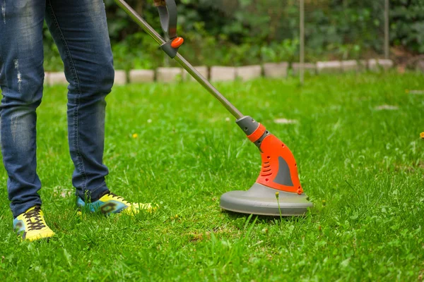 Young worker with a string lawn trimmer mower cutting grass in a blurred nature background — Stock Photo, Image