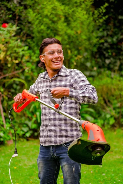 Close up of young worker wearing transparent glasses protection and holding a lawn trimmer mower cutting grass in a blurred nature background — Stock Photo, Image