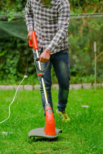 Outdoor view of young worker using a lawn trimmer mower cutting grass in a blurred nature background — Stock Photo, Image