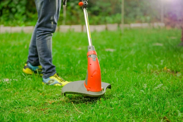 Young worker wearing jeans and using a lawn trimmer mower cutting grass in a blurred nature background — Stock Photo, Image