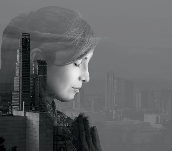 Side view of beautiful woman praying with her eyes close with doble exposure of a city landscape, in a white background, black and white effect