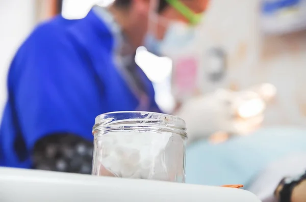 Close-up de frasco com algodão com um dentista médico desfocado atrás, trabalhando em um paciente — Fotografia de Stock