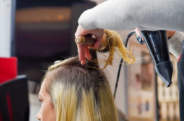 Arka plan bulanık saç kurutma makinesi ve yuvarlak fırça ile sarışın saç kurutma bir saç stilist yakın çekim — Stok fotoğraf