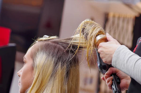 Detailní záběr z kadeřníků sušení blond vlasy s vlasy Fén a kulatý kartáč v rozmazané pozadí — Stock fotografie