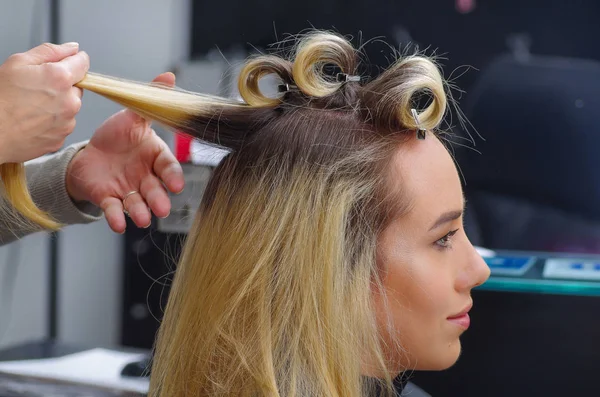 Porträtt av vacker kvinna i en frisersalong med en stylist arbetar med papiljotter i huvudet, i en hår salong bakgrund — Stockfoto