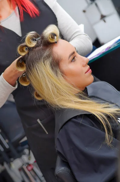 Curlers kafasına saç salonu arka planda çalışan bir stilist ile bir kuaför salonu içinde güzel kadın yakın çekim — Stok fotoğraf