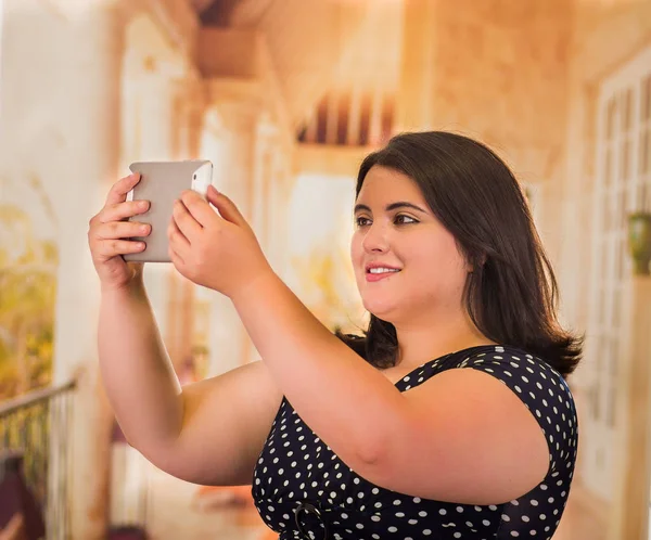Retrato de una hermosa mujer gorda en un hermoso vestido, tomándose una selfie usando la tableta en un fondo borroso —  Fotos de Stock