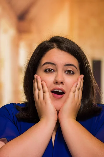 Portrait of young beautiful woman in a blue dress, with both hands under her chin on blurred background — Stock Photo, Image