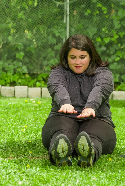 Mladá žena, která dělá jóga cvičení v přírodě, posezení v zemi snaží dotknout nohou s oběma rukama v zahradě pozadí — Stock fotografie