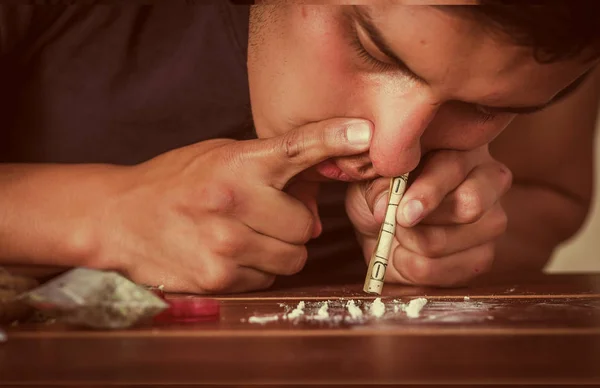 Закрыть человека наркомана с помощью обернутой долларовой купюры, вдыхающей кокаин, приготовленной над деревянным столом, жизненный эффект — стоковое фото