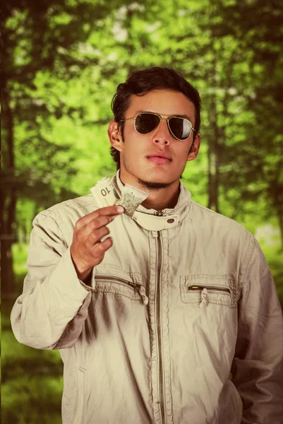Close up of a man dealer wearing dark sunglases, and holding in his hands money and drug, trafficking, crime, in a blurred background, vintage effect — Stock Photo, Image