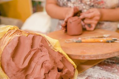 Bir kil kitle heykel Atölyesi, arka plan bulanık ahşap tablo üzerinde çalışan arkasında bir bulanık kadın ustası ile yakın çekim