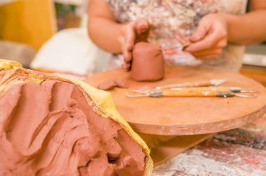 Bir kil kitle heykel Atölyesi, arka plan bulanık ahşap tablo üzerinde çalışan arkasında bir bulanık kadın ustası ile yakın çekim