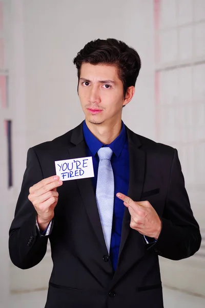 Sad business man holding a paper of youre fired text on it, in a blurred background